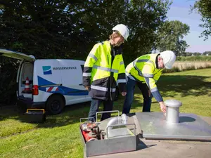 Zwei Fachkräfte vom Wasserservice Westfalen Weser bei Wartungsarbeiten an einer unterirdischen Anlage auf einer Grünfläche.