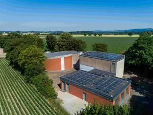 Luftaufnahme eines Betriebsgebäudes mit Photovoltaikanlagen auf dem Dach, umgeben von Feldern und Bäumen.